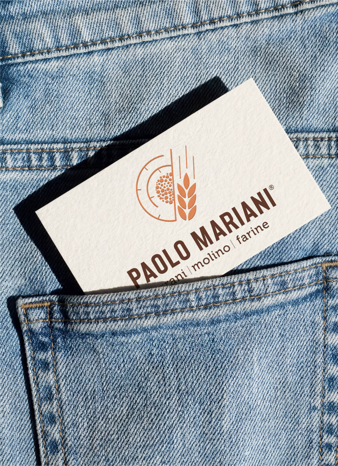 Business card with logo and text 'PAOLO MARIANI' partially inside a light blue denim jeans back pocket.