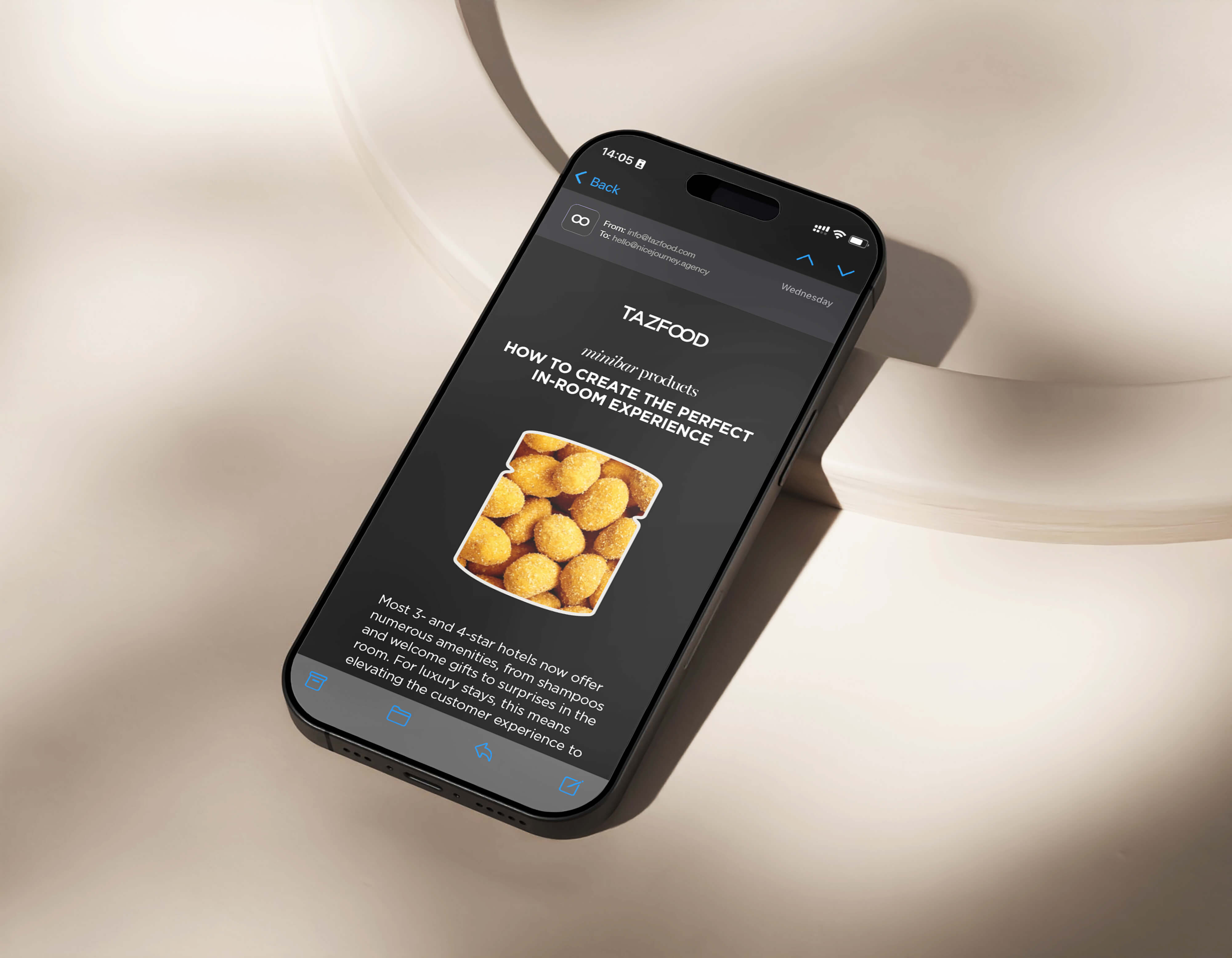 Smartphone displaying an email from TAZFOOD about minibar products titled 'How to create the perfect in-room experience' with an image of coated nuts and partial text about hotel amenities.